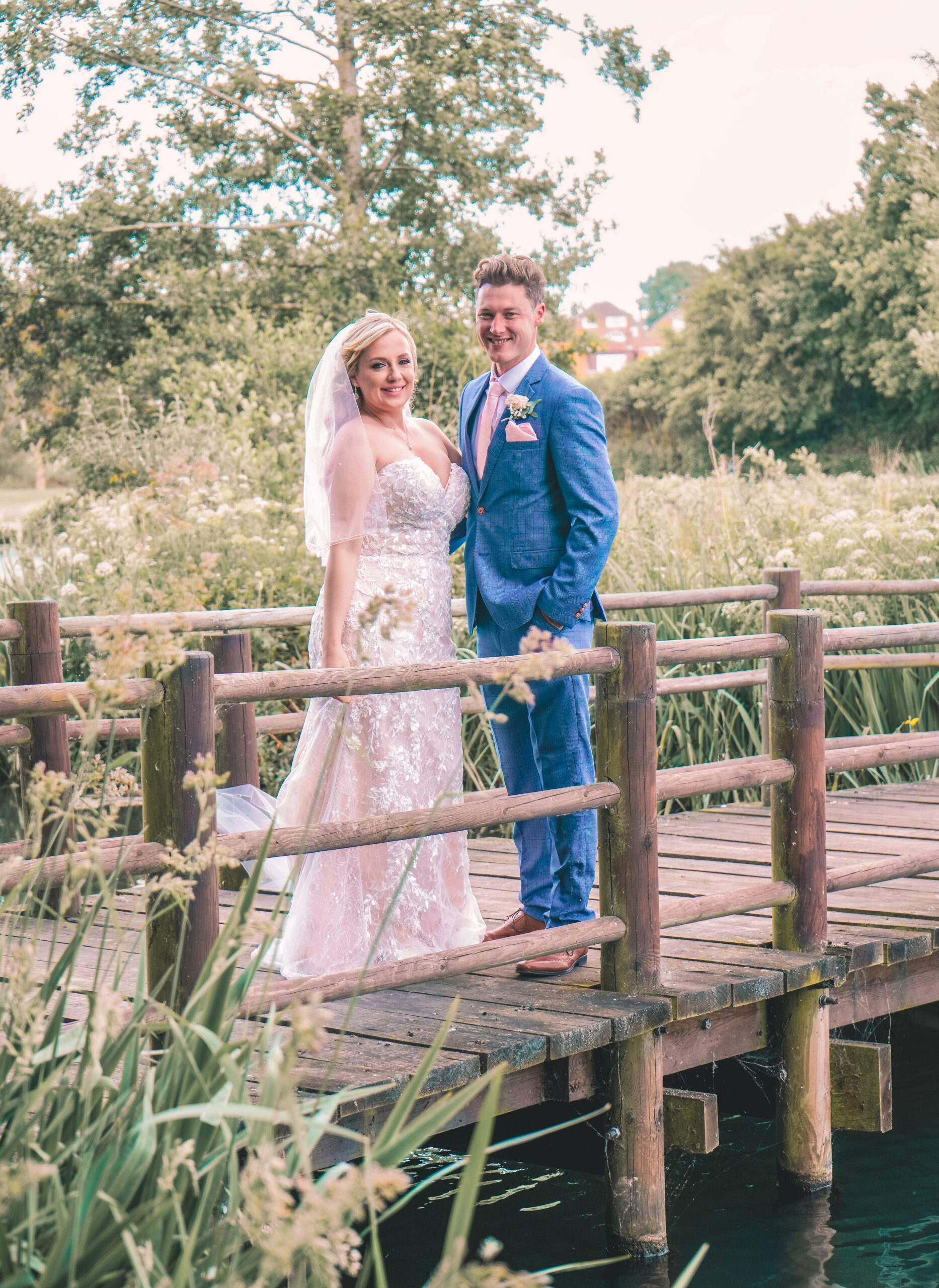 Bride in blush and groom in a blue suit by a wooden footbridge, part of my Bursledon wedding photographer prices and packages