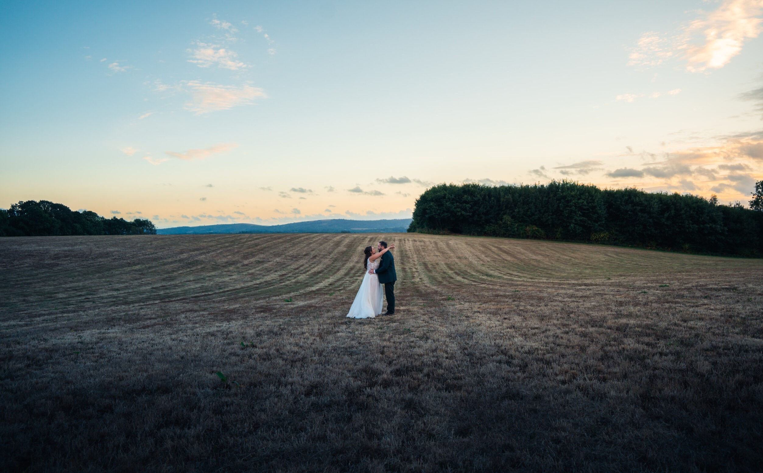 Couple standing in an open field at sunset, one of a set of golden hour wedding photos