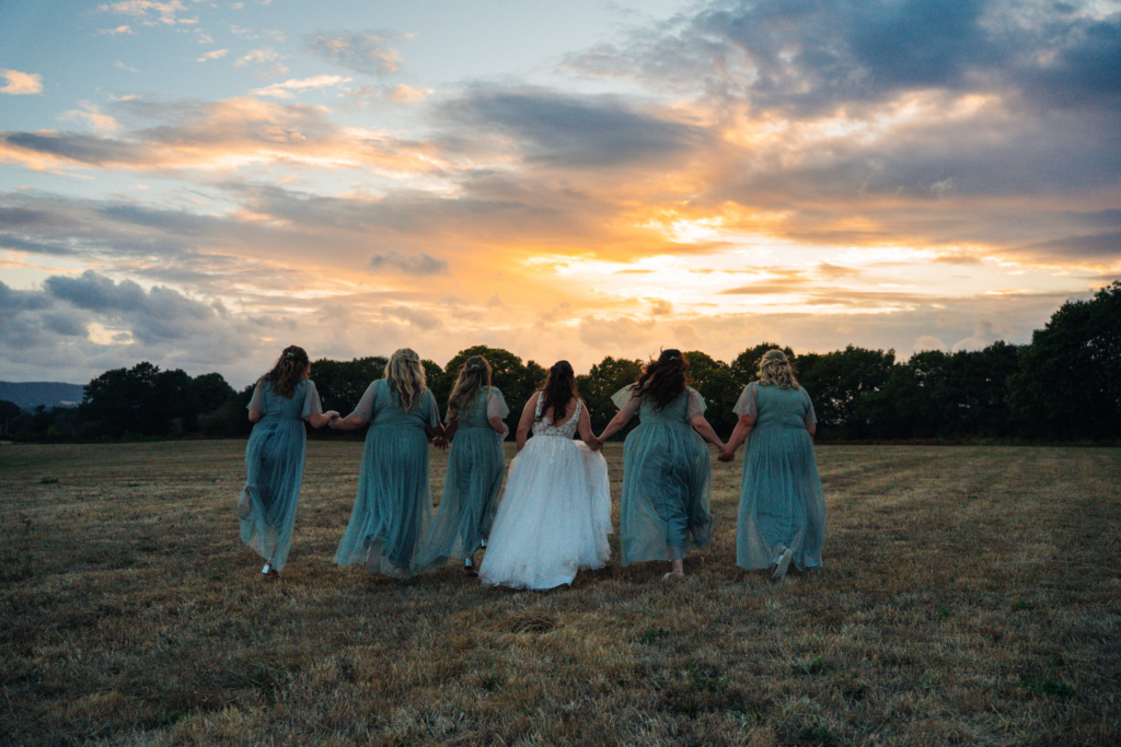 Bride and bridesmaids walking through a field at sunset, a moment captured for a wedding highlight video
