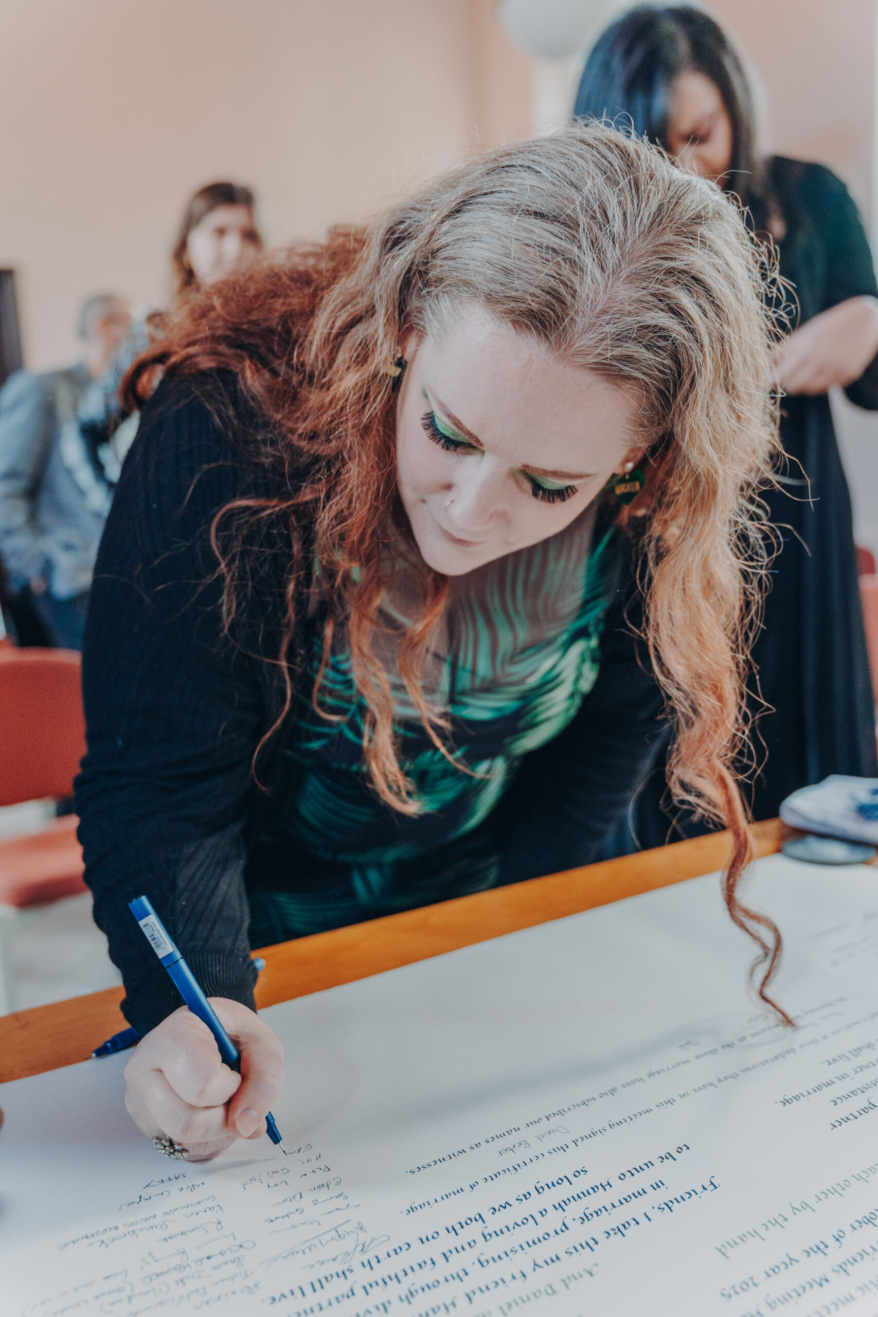 Guest writing a message in the guestbook, wedding stationery and details secured with a wedding photographer deposit