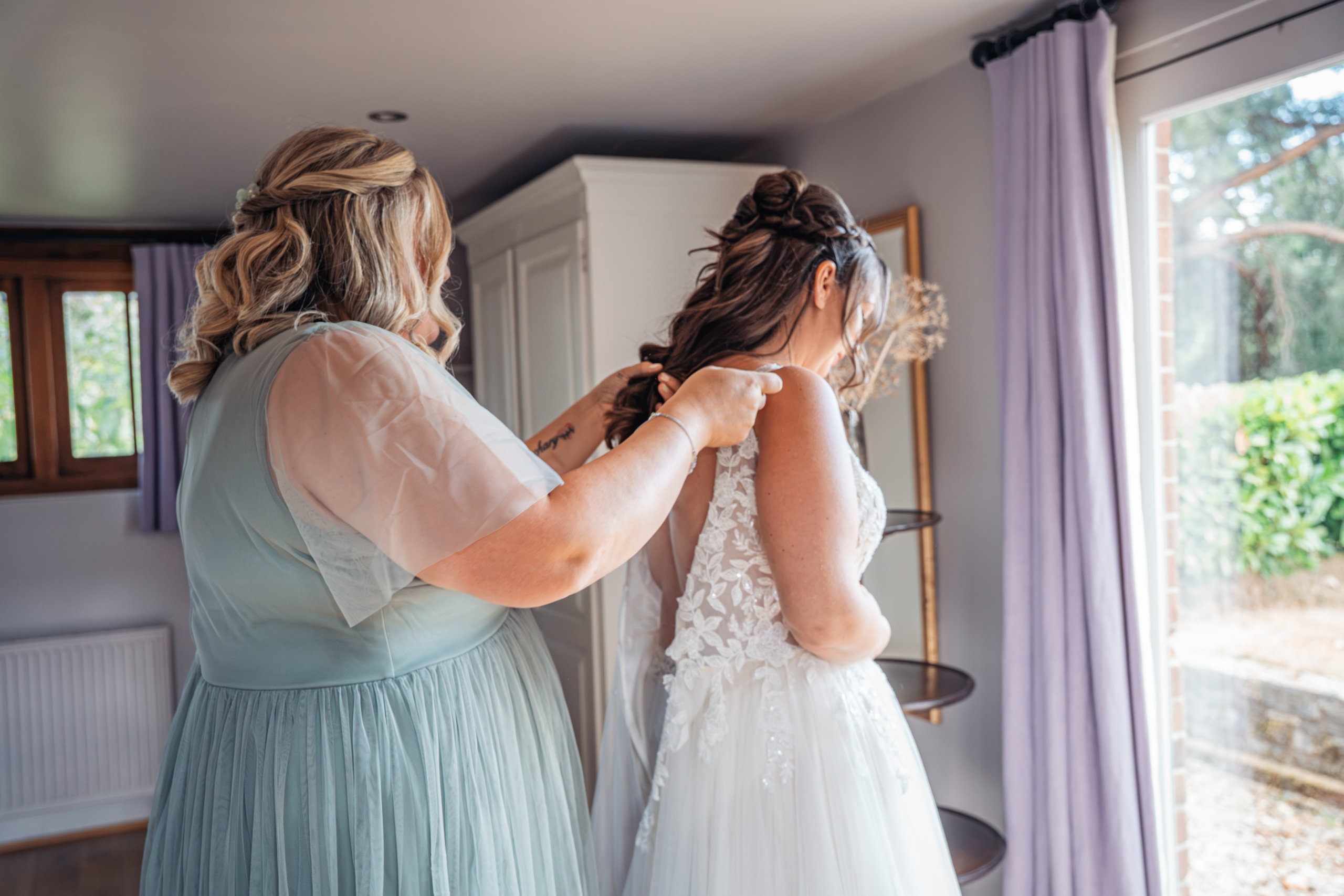 A bridesmaid fastening the bride’s dress on a Hampshire wedding morning