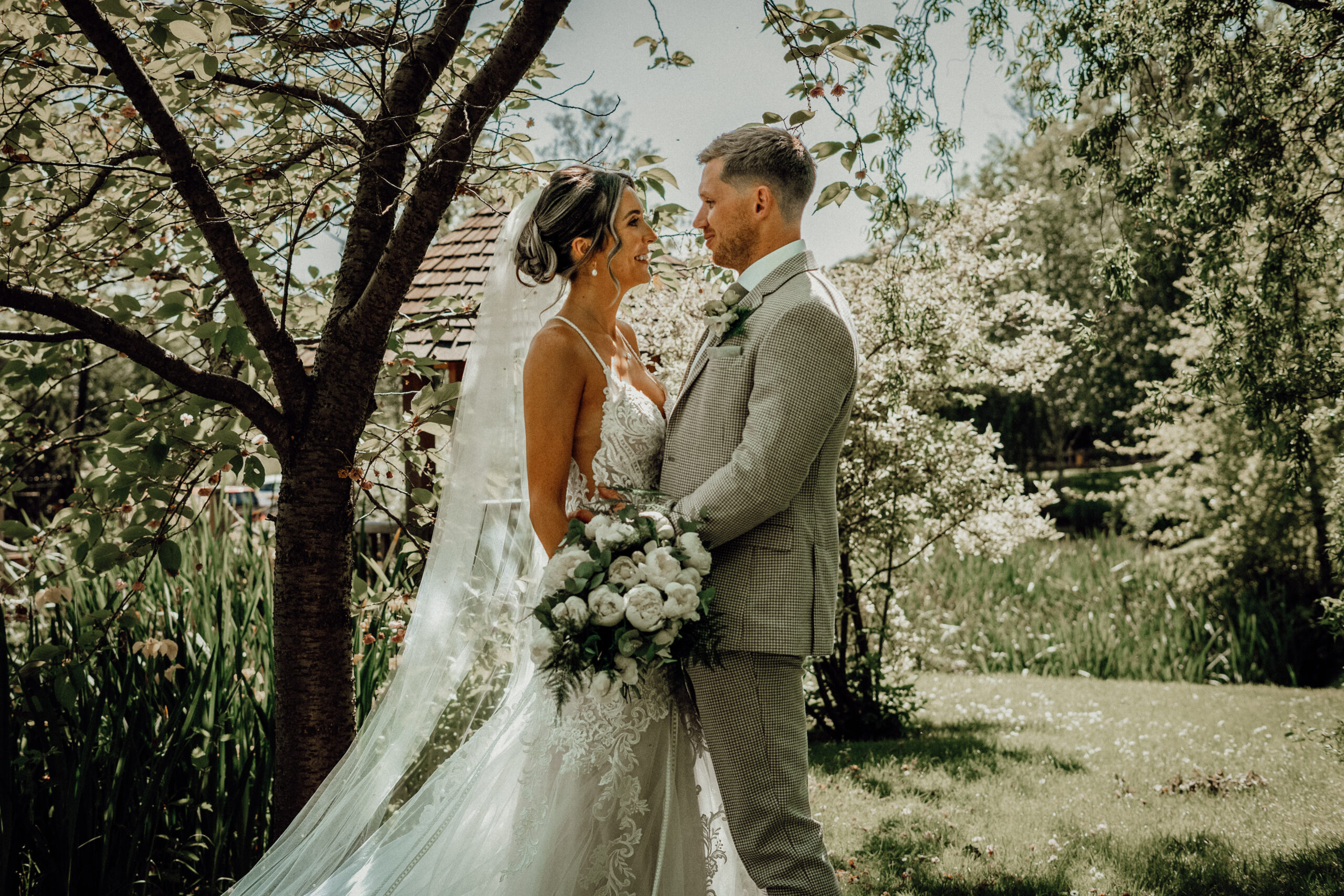 Bride and groom facing each other beneath a tree, bouquet in hand, photographed by a wedding photographer in Bedhampton