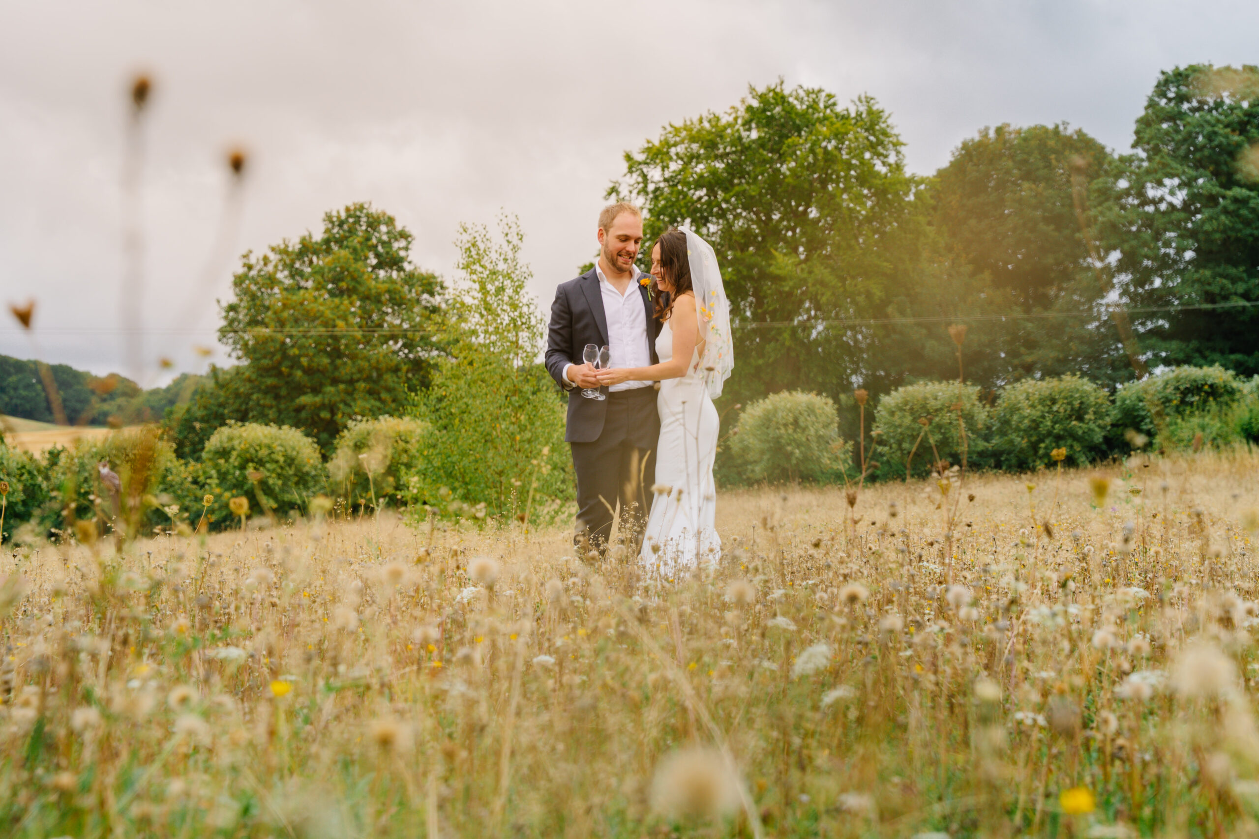 Bride and groom standing in a summer meadow, captured by a wedding photographer in Bedhampton