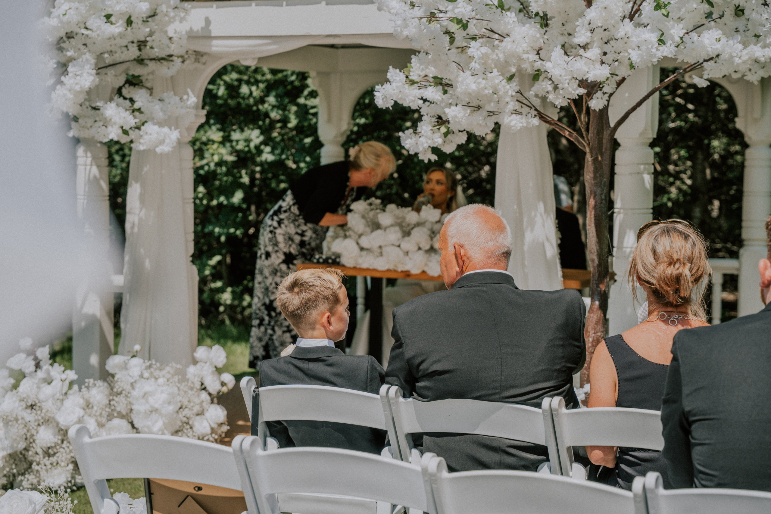 Guests watching the ceremony beneath a white floral arch