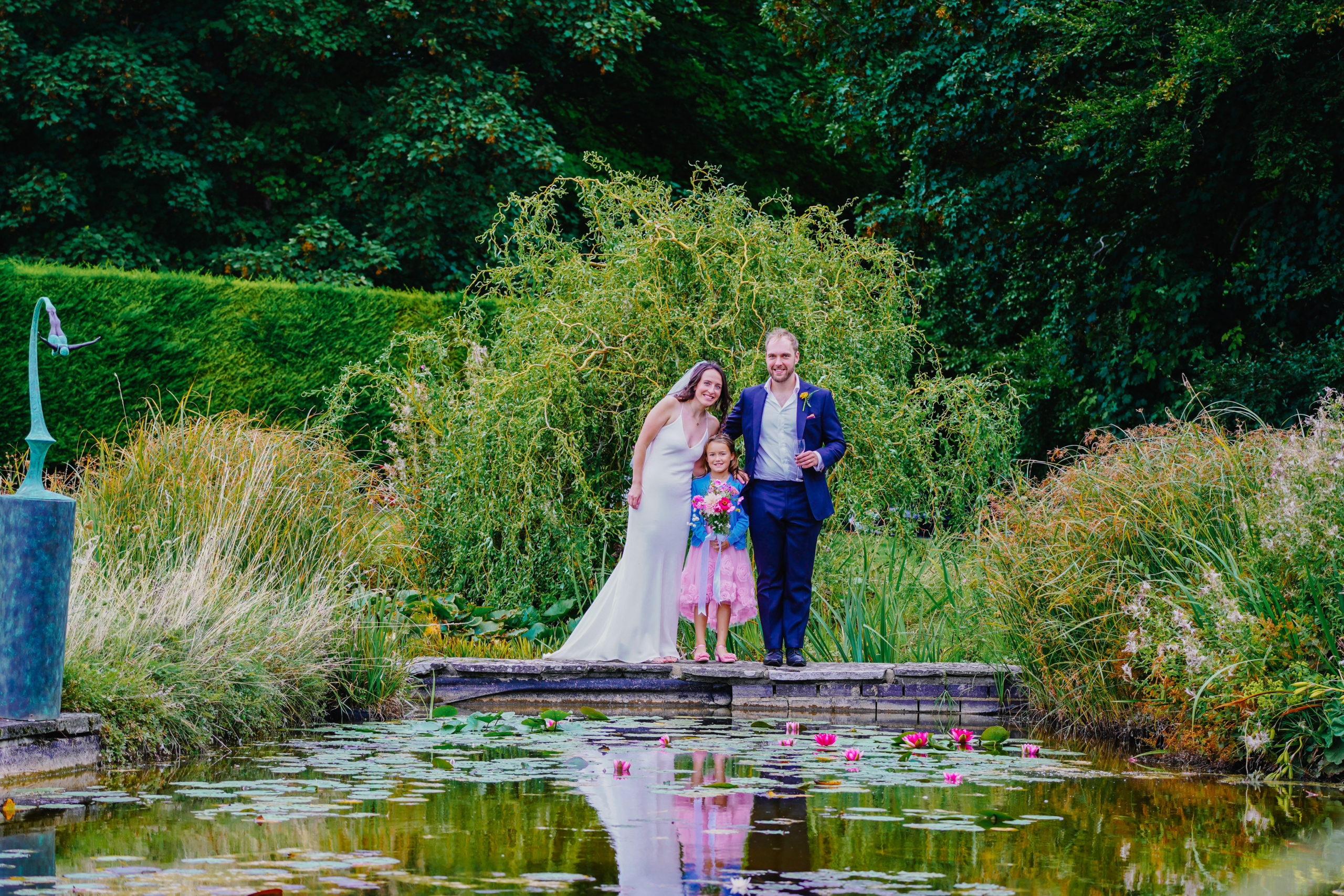 The couple standing on a bridge above a garden lily pond
