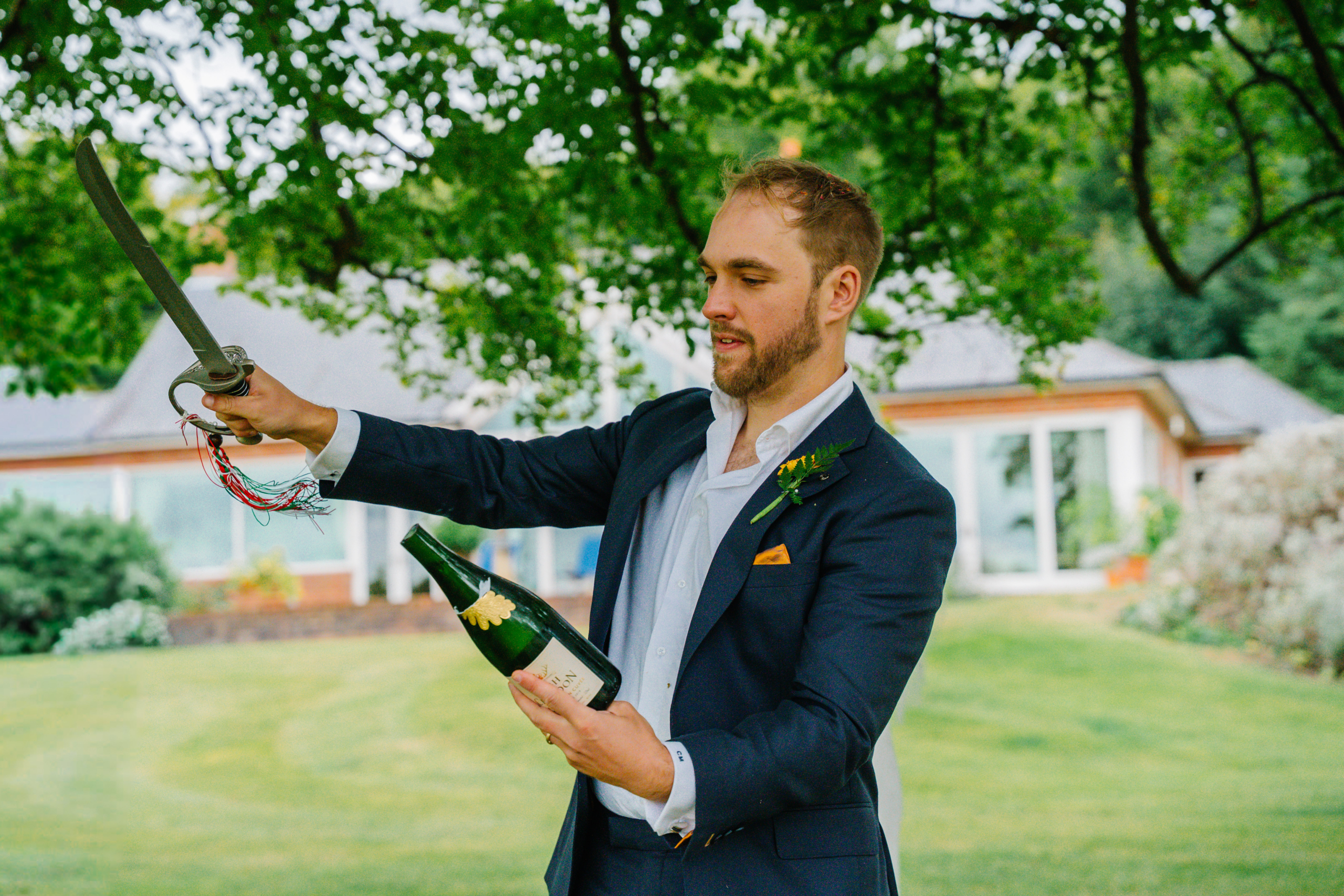 The groom popping a bottle of champagne in the garden